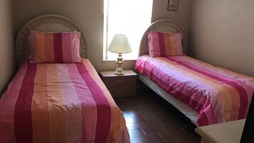Une chambre à coucher avec deux lits, chacun doté de draps à rayures, une table de chevet avec une lampe et une fenêtre avec des rideaux.