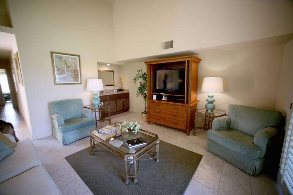 A living room with two light blue sofas, a glass coffee table, a wooden cabinet with a television, and two lamps on side tables.