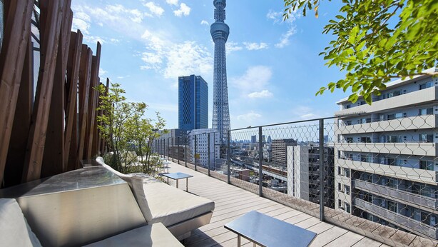 A rooftop terrace with a view of the Tokyo Tower, a modern building, and a chain-link fence. - ONE＠Tokyo by insomnia (Tokyo)