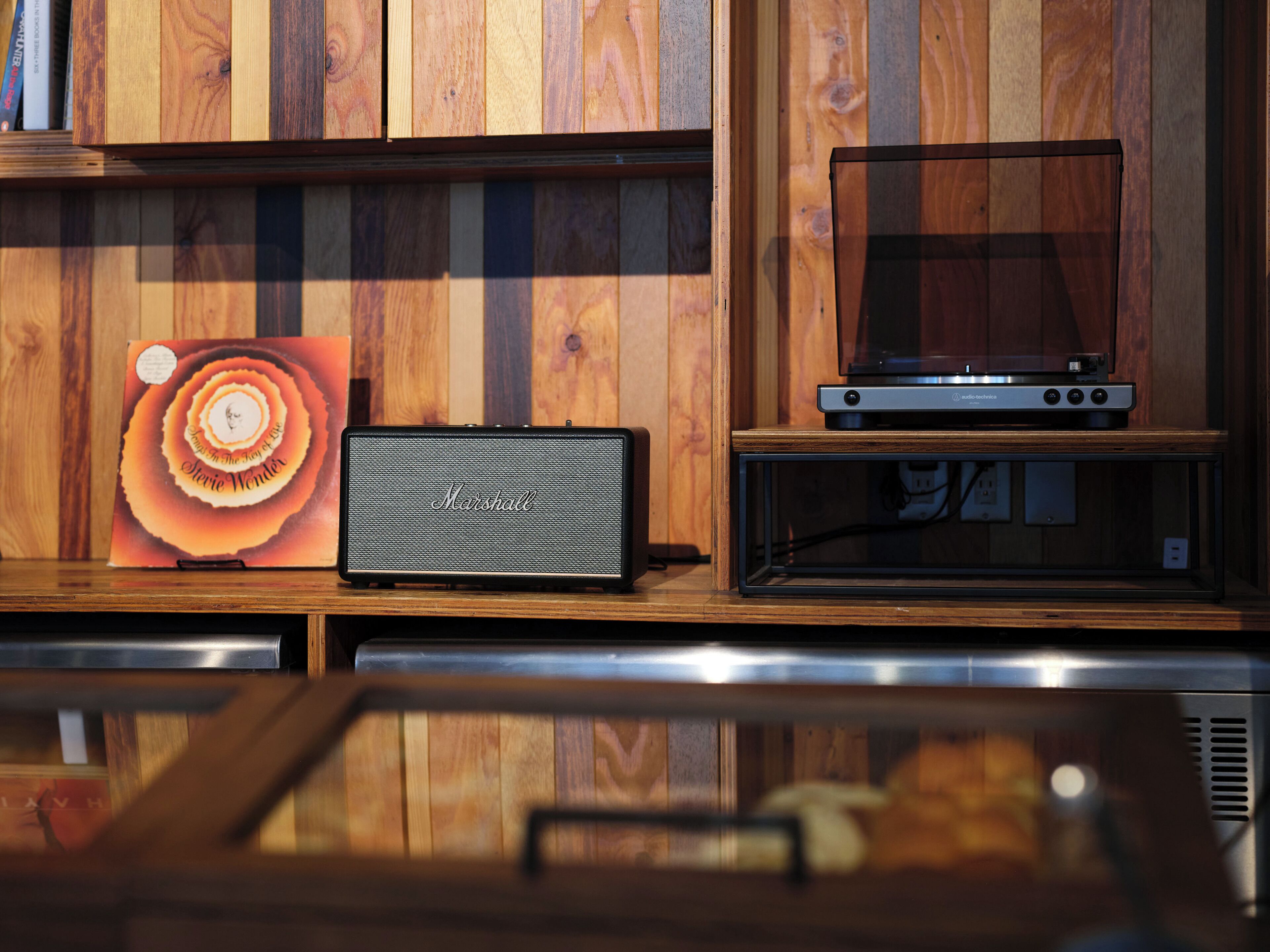 Puinen seinä, jossa on kaiutin ja levysoitin hyllyllä.