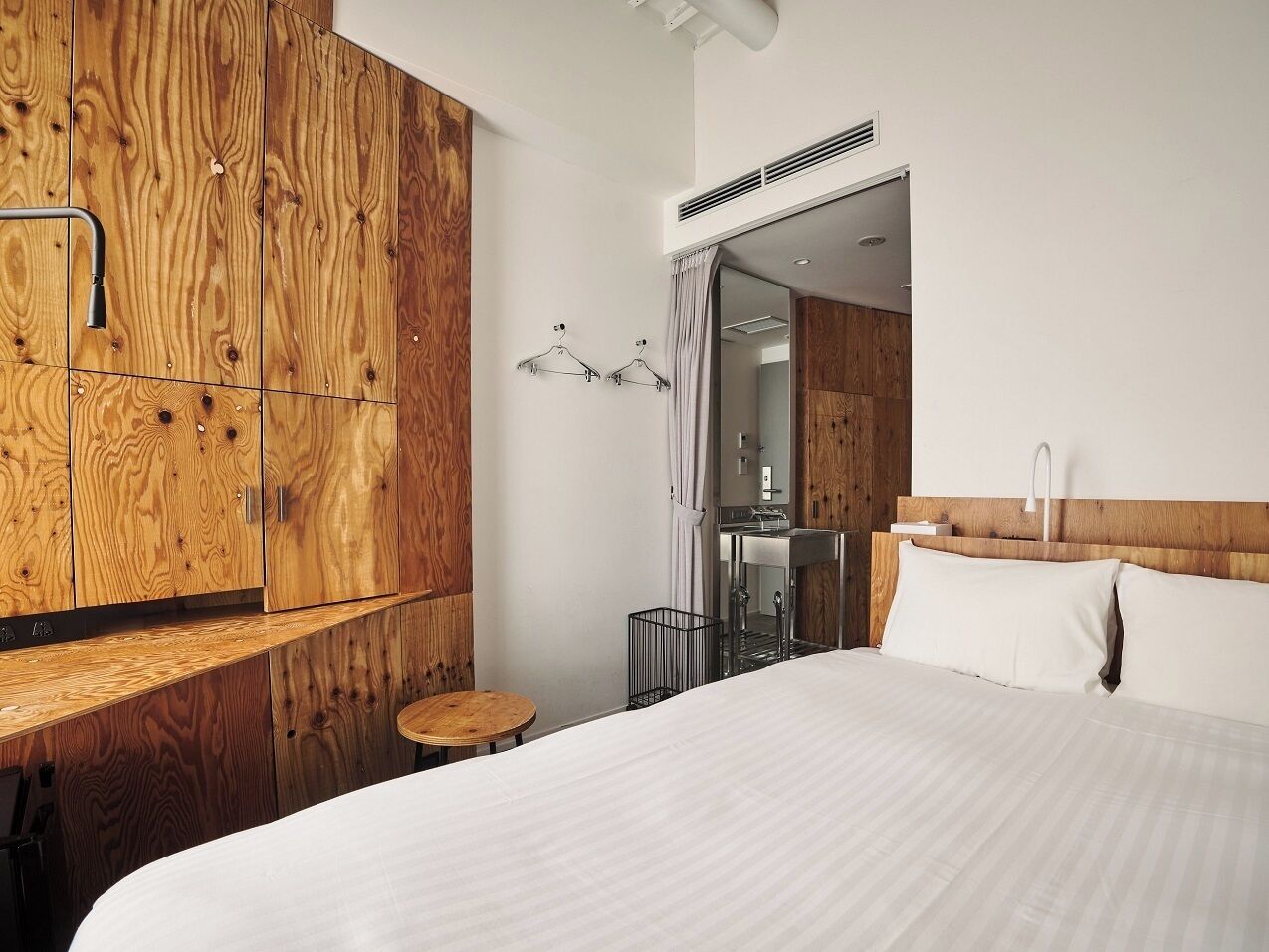Habitación de hotel con armario de madera, cama con ropa blanca, una mesita redonda y un espejo.