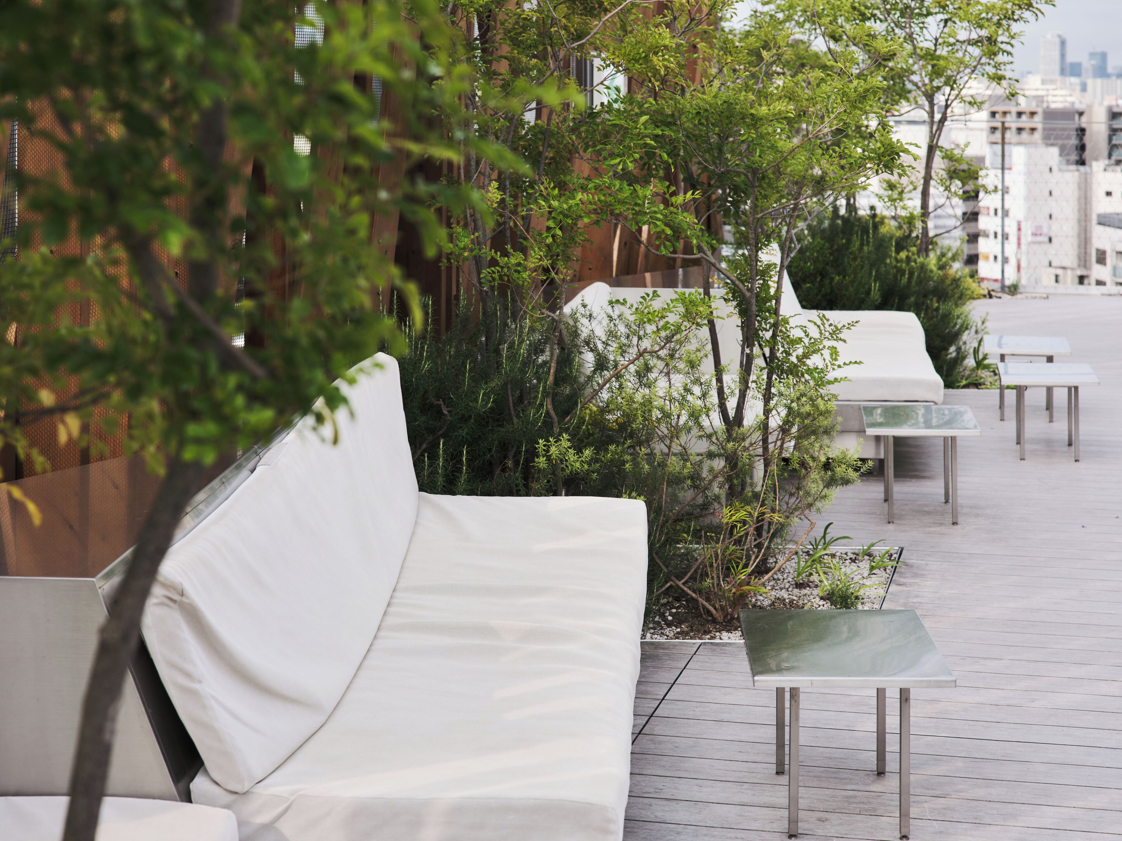 Outdoor seating with white cushions, a glass table, and greenery.