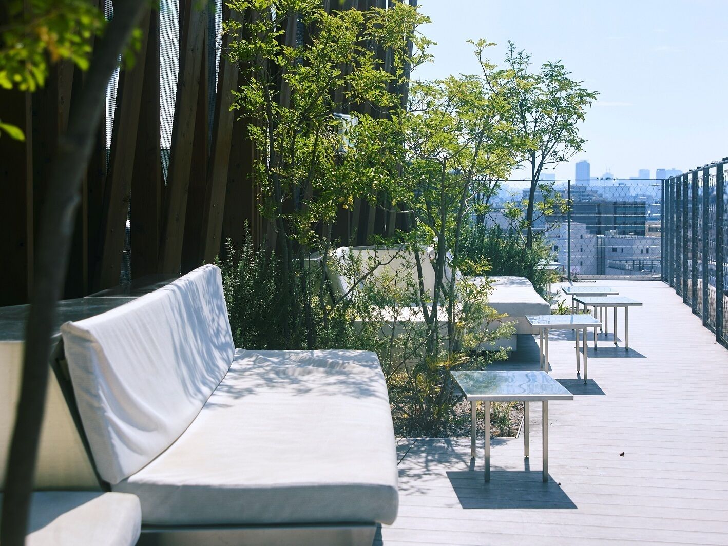 Terraza en la azotea con sofá blanco, mesas y plantas, con vistas a un paisaje urbano.