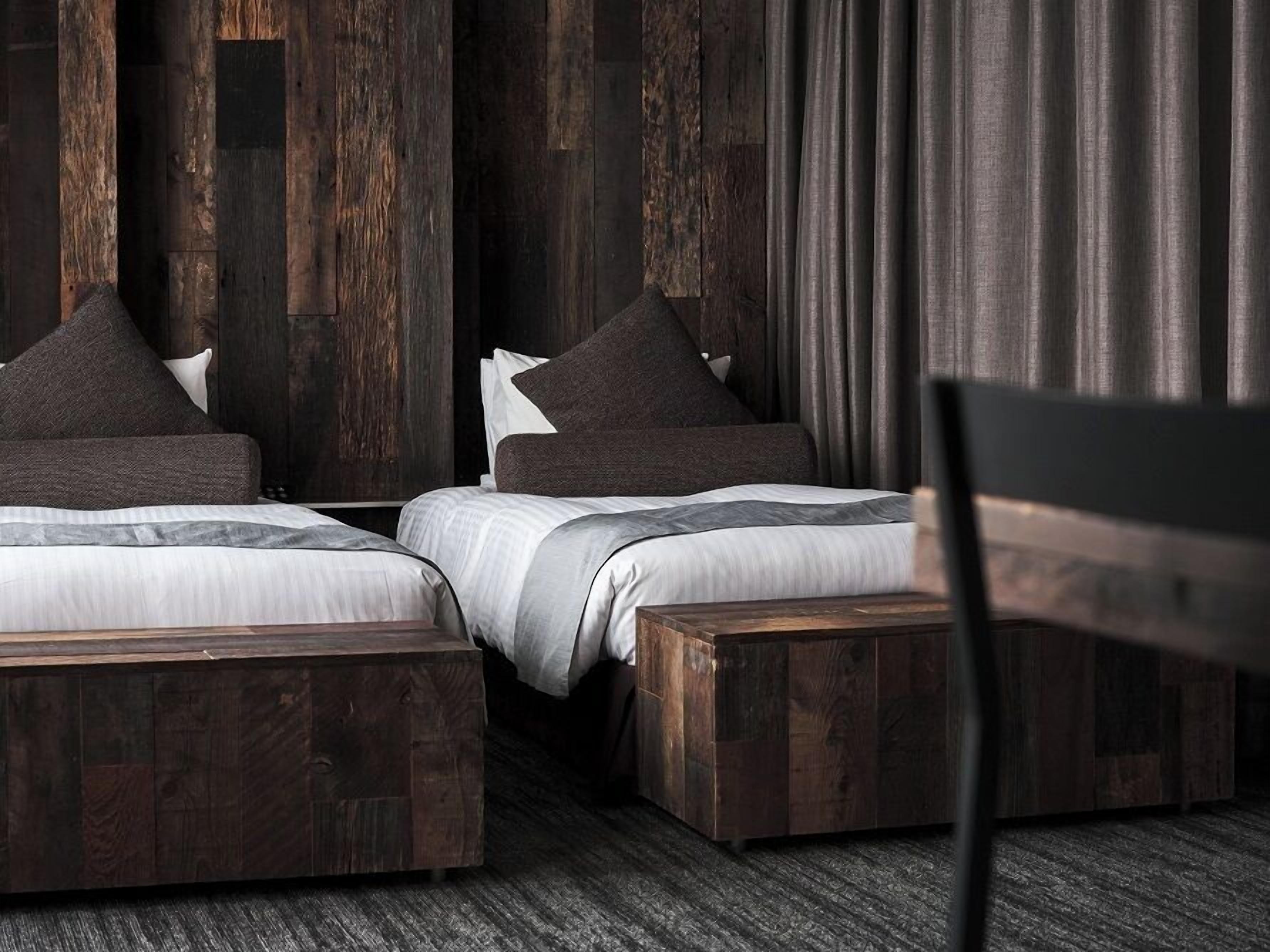A bedroom with two beds, dark wooden headboards, and a chair.