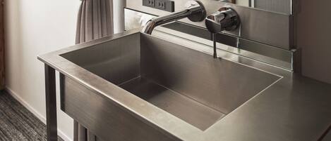 A modern bathroom with a stainless steel sink, a mirror, and a towel rack.