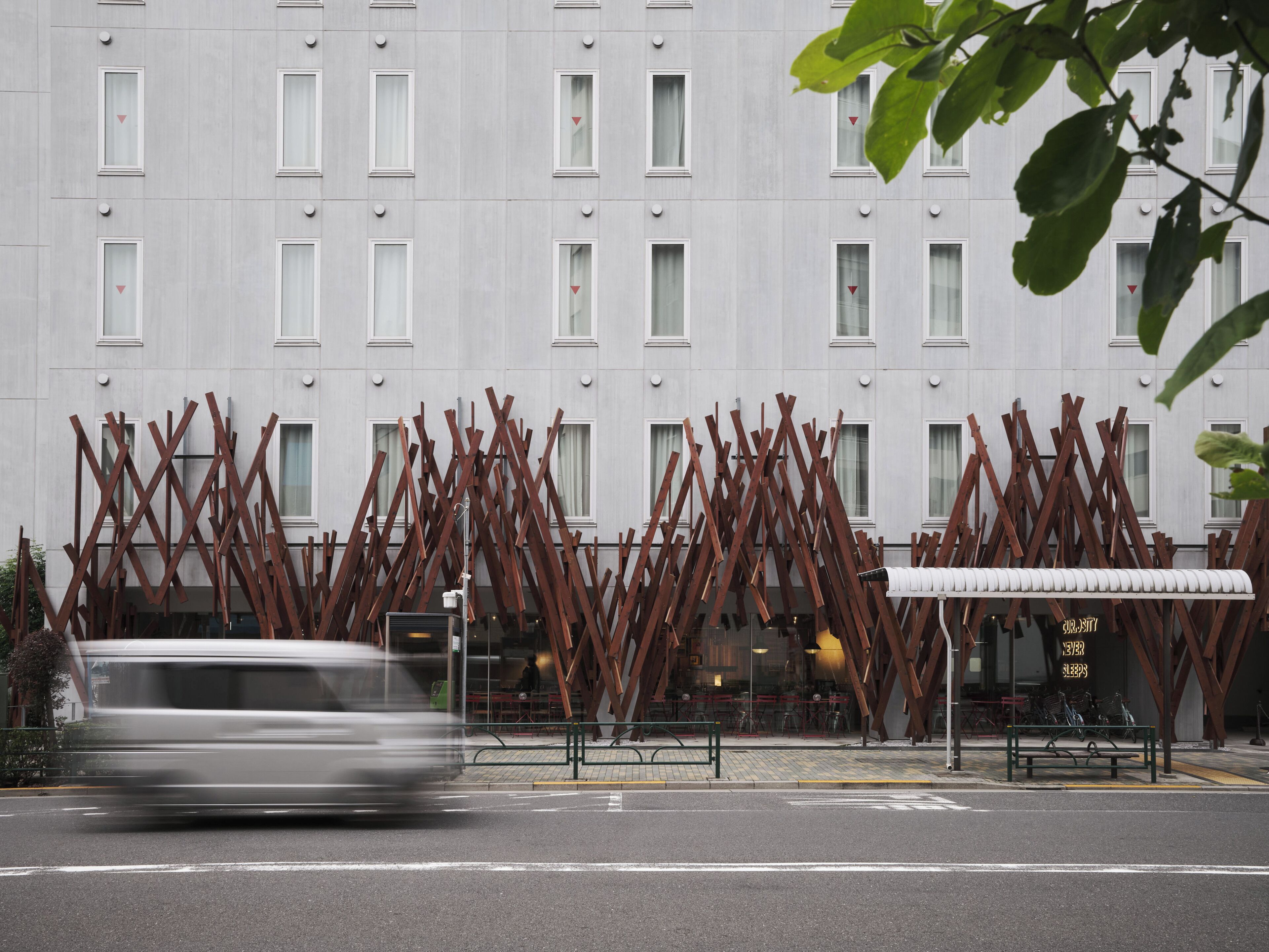 A building with a modern facade, a bus stop, and a street with a moving vehicle.