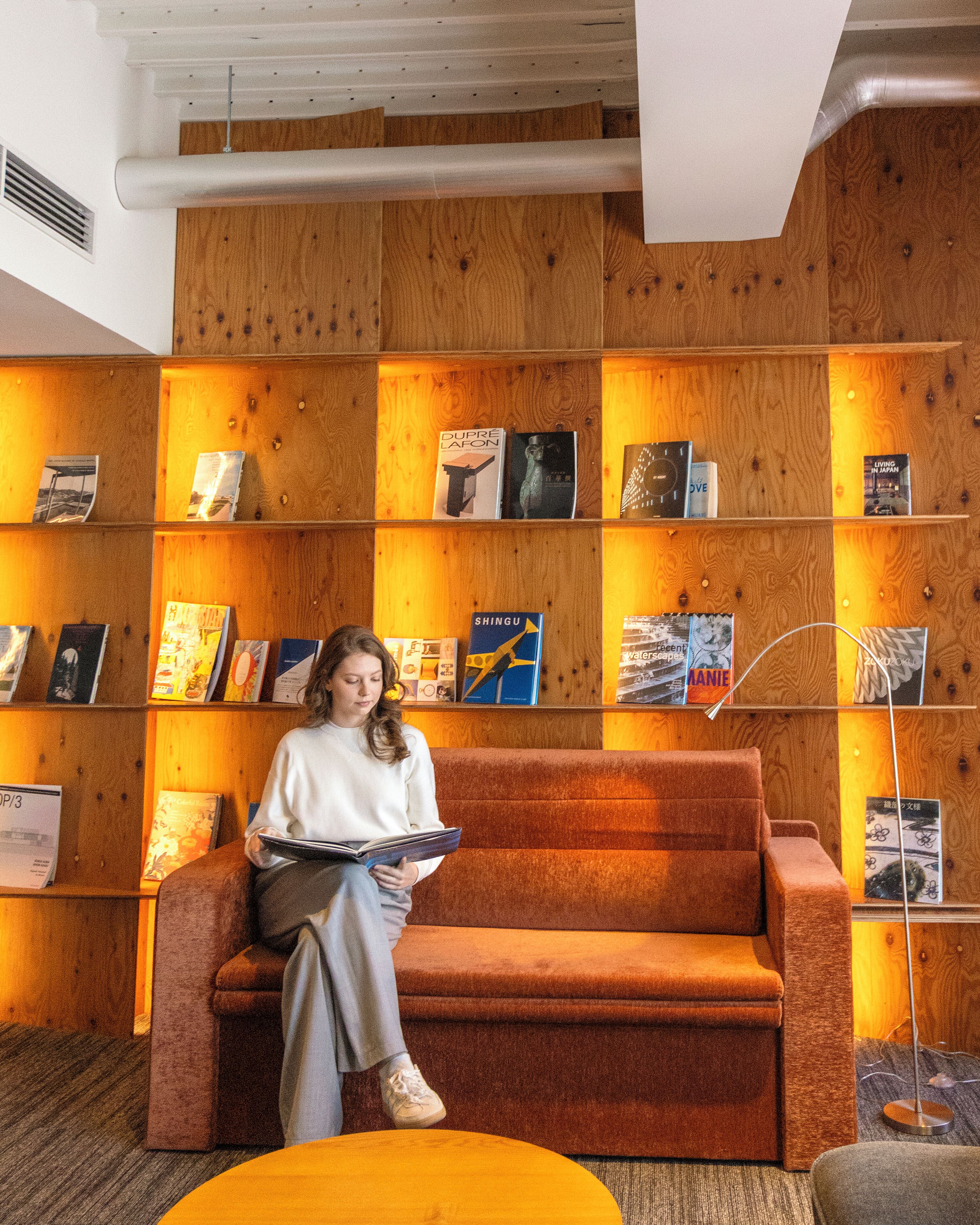 A person seated on a sofa in a room with wooden panel walls, reading a book.