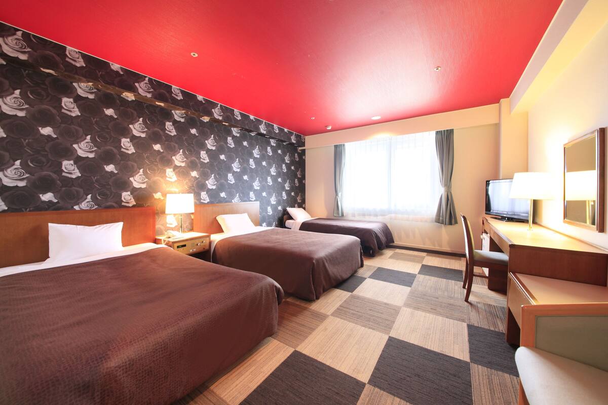 Habitación de hotel con dos camas, un escritorio, una silla, un televisor y una ventana con cortinas.