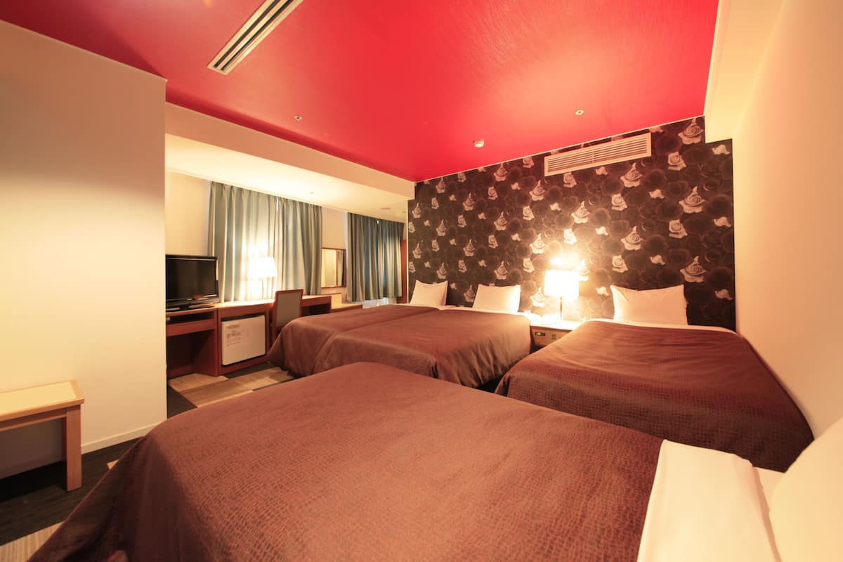 Habitación de hotel con dos camas, un escritorio, un televisor y una ventana con cortinas.