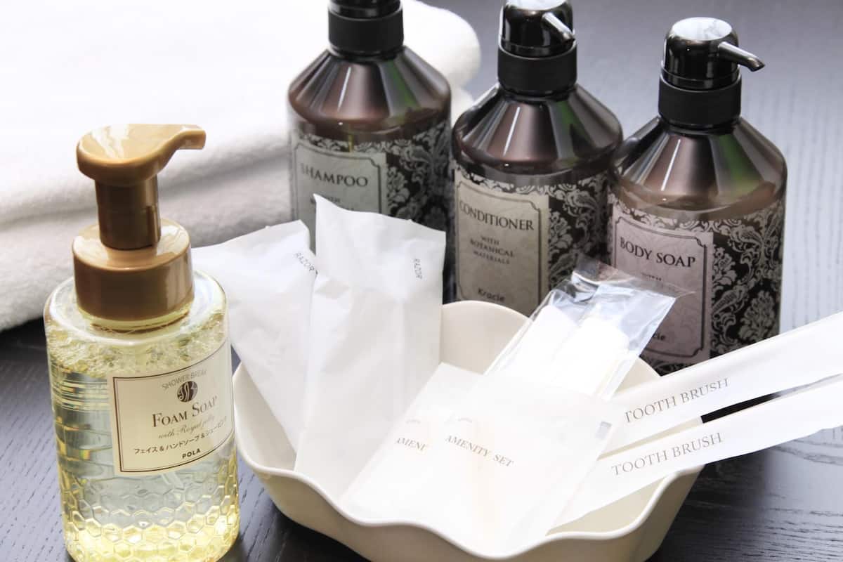 A set of toiletries including a bottle of foam soap, shampoo, conditioner, and body soap, along with two toothbrushes and a tissue box.