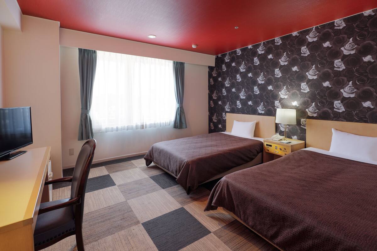 Habitación de hotel con dos camas, un escritorio, un televisor y una ventana con cortinas.