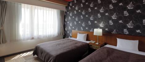 Habitación de hotel con dos camas, una mesita de noche con lámpara, pared estampada y ventana con cortinas translúcidas.