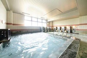 Una gran piscina interior con agua cristalina, paredes de azulejos y un techo alto.