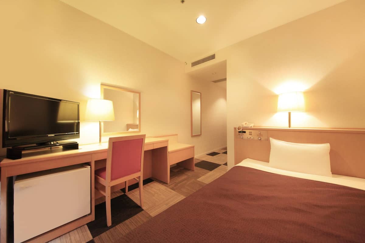 Una habitación de hotel con cama, escritorio, televisor y refrigerador.
