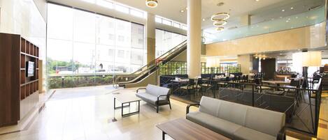 A spacious lobby with a central seating area, an escalator, and a large window providing a view of the outside.