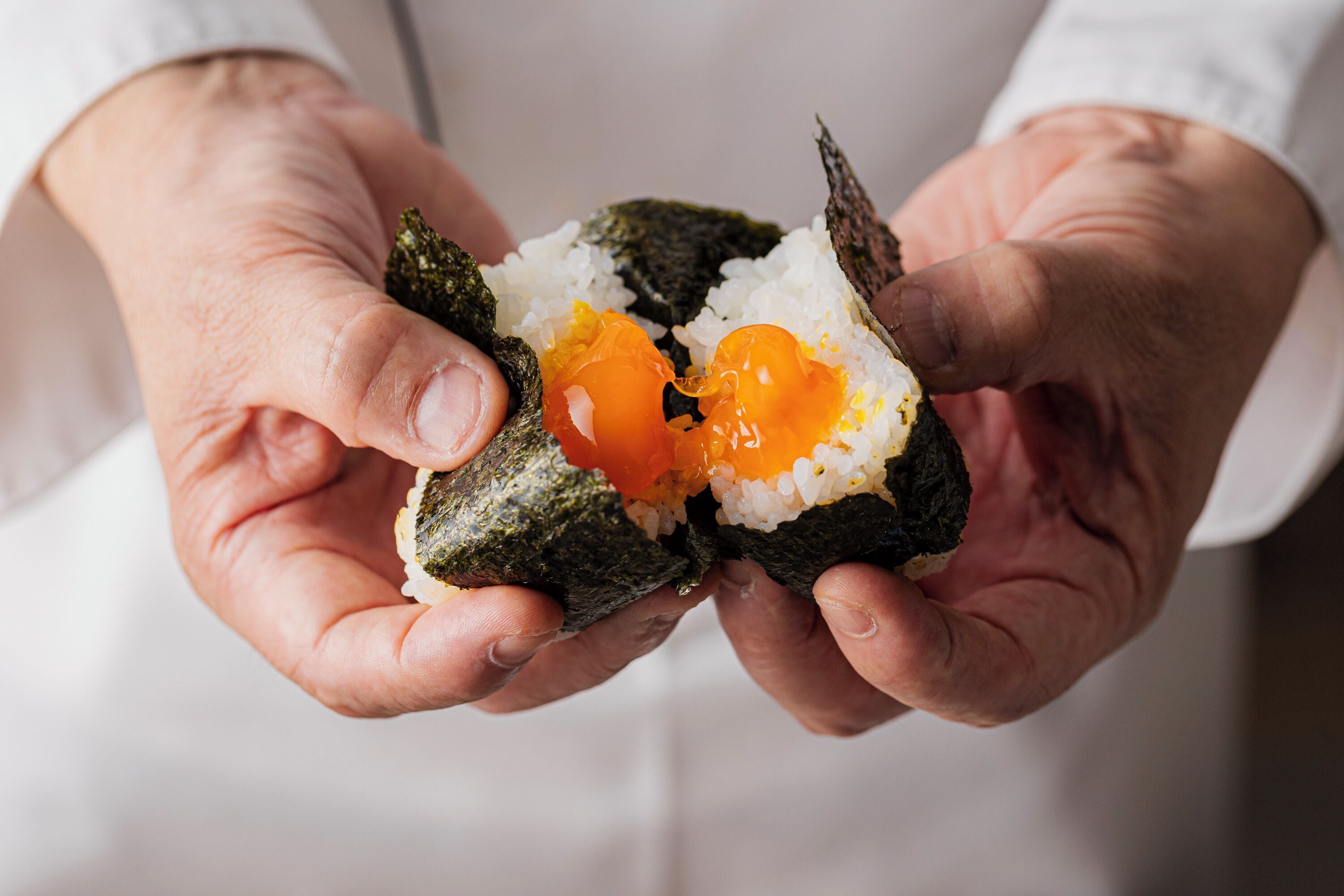 Una persona sosteniendo un rollo de sushi con arroz y huevo visibles.