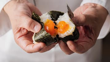 Eine Person hält eine Sushi-Rolle mit sichtbarem Reis und Ei.