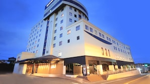 Un hotel de varios pisos con fachada curva, una entrada destacada con escalones y un letrero que indica que es un hotel.