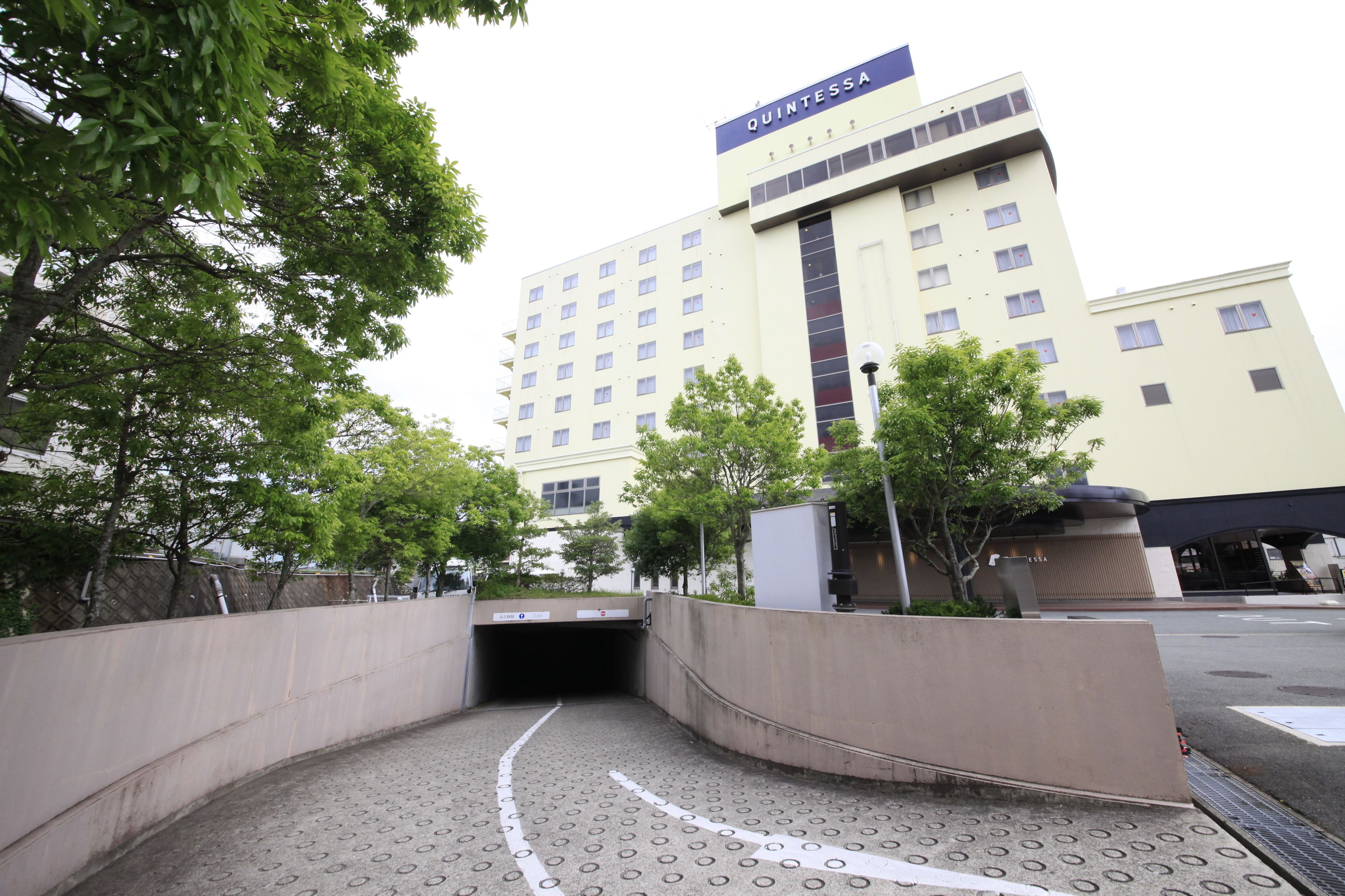 A hotel entrance with a ramp leading to a tunnel, surrounded by trees and a concrete wall.