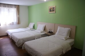 Een hotelkamer met drie enkele bedden, een nachtkastje met een lamp, een schilderij aan de muur en een raam met gordijnen.