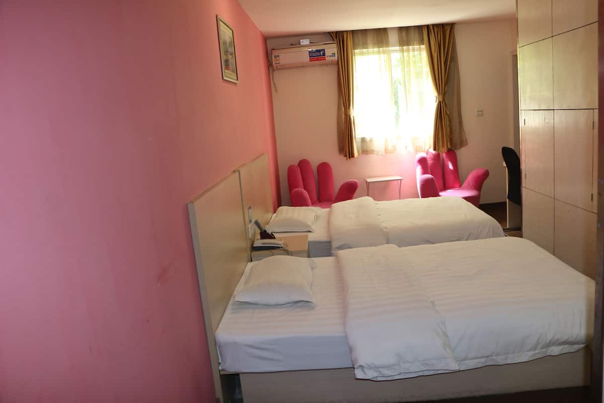 Quarto de hotel com duas camas, uma escrivaninha, uma cadeira e um guarda-roupa.