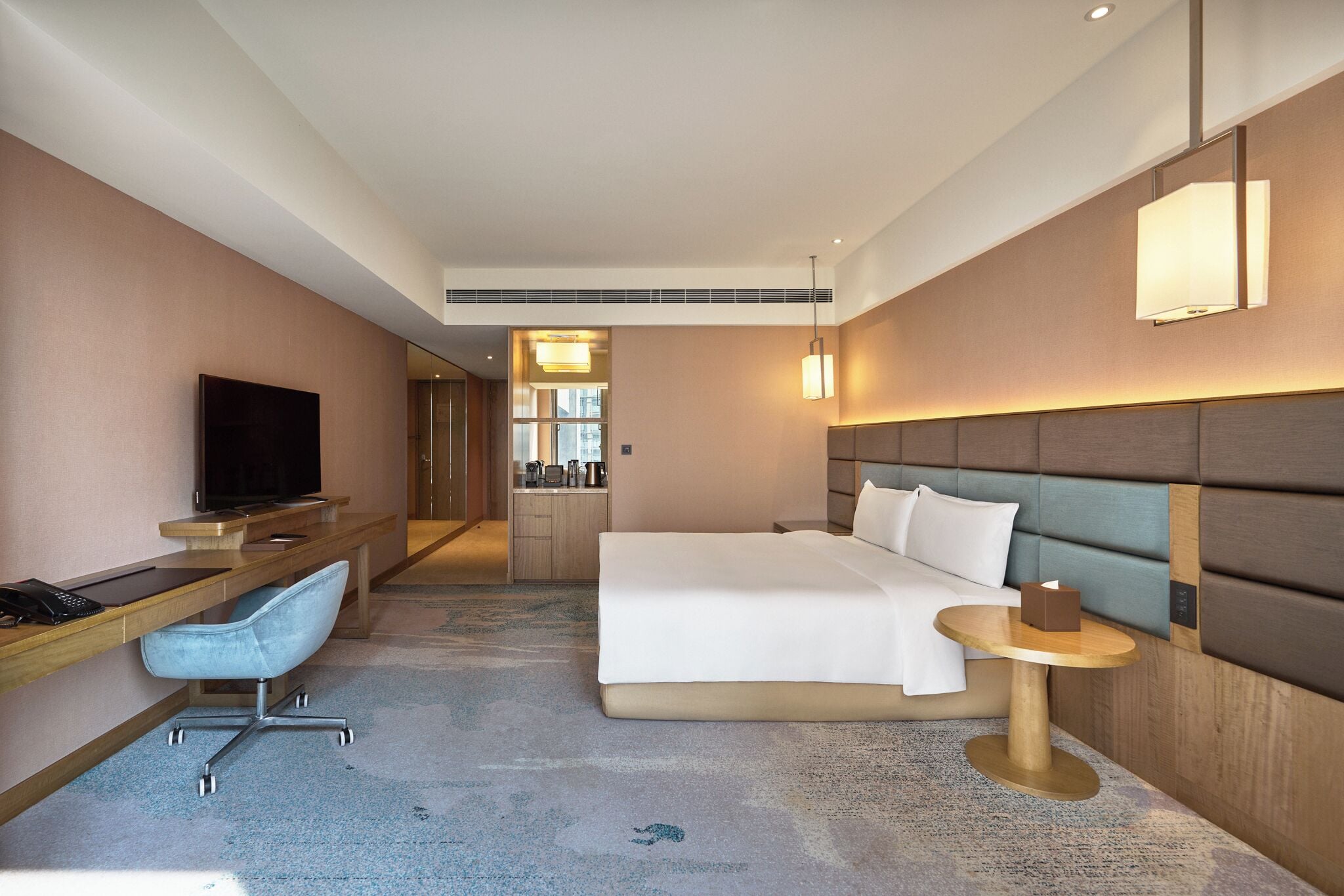 Habitación de hotel con cama, escritorio, silla, televisor, mesita de noche y lámpara.