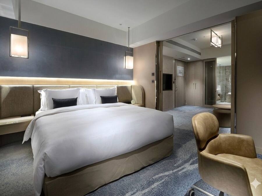 A hotel room with a large bed, a bedside table, a chair, a mirror, and a wardrobe.