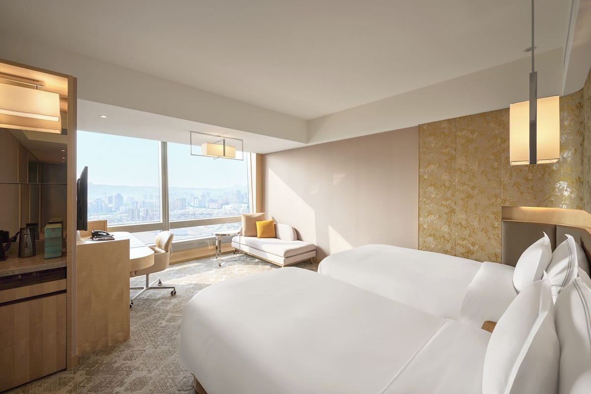 Quarto de hotel com uma cama grande, uma escrivaninha, um sofá e vista para a cidade.