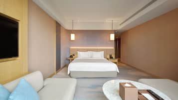 A hotel room with a bed, a sofa, a TV, a bedside table, and a nightstand.
