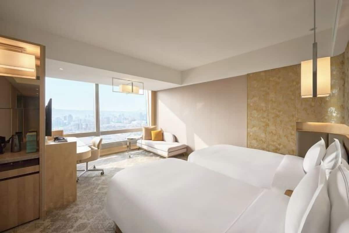 Quarto de hotel moderno com uma cama grande, uma escrivaninha, uma cadeira e vista para a cidade.