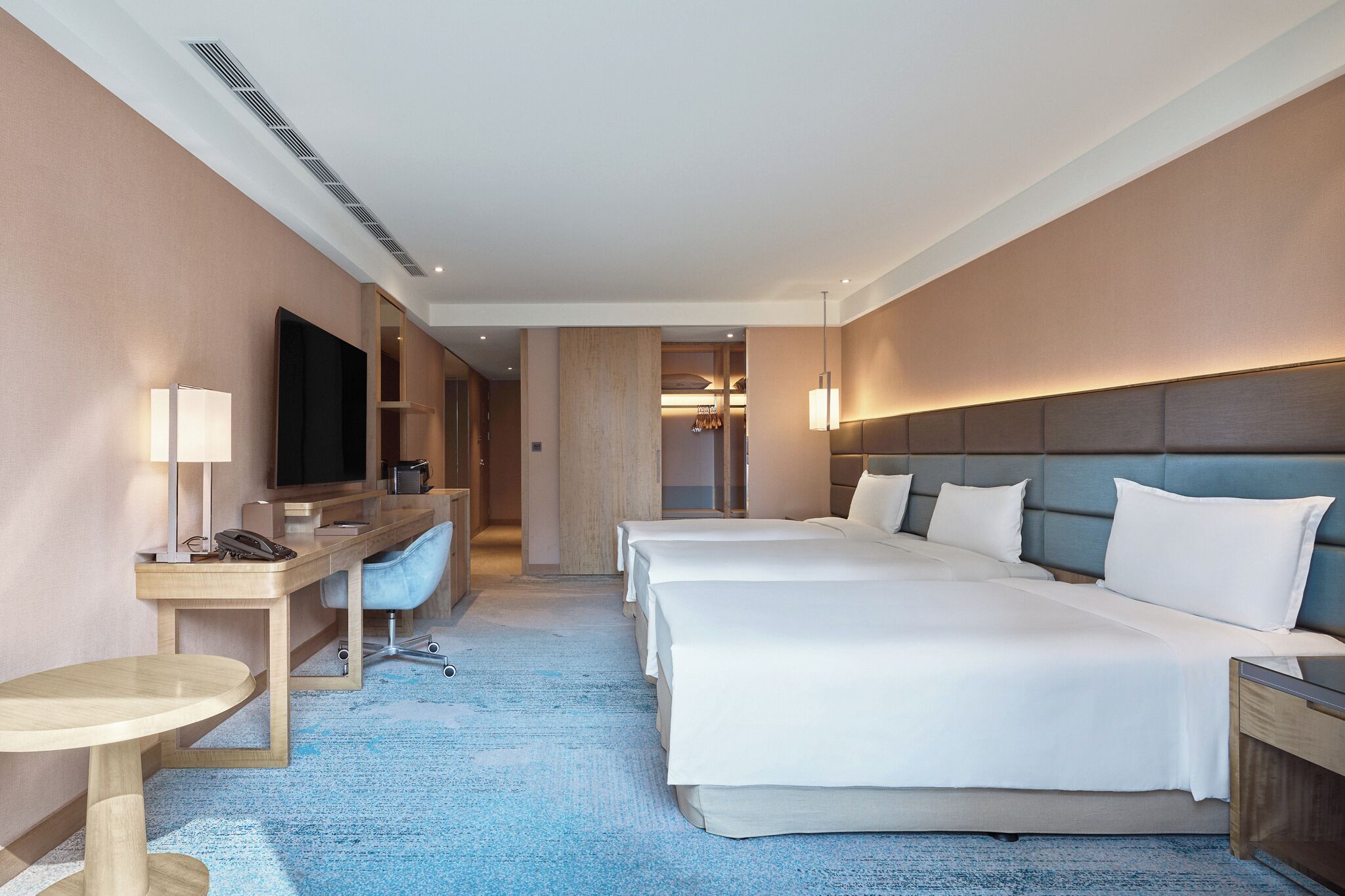 A hotel room with a large bed, a desk with a chair, a TV, and a bedside table.