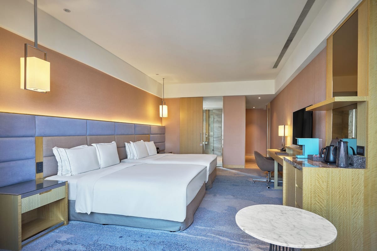 Quarto de hotel com cama grande, mesas de cabeceira, escrivaninha, cadeira e uma mesinha redonda.