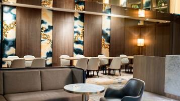 A hotel lobby with a seating area, tables, and a reception desk.