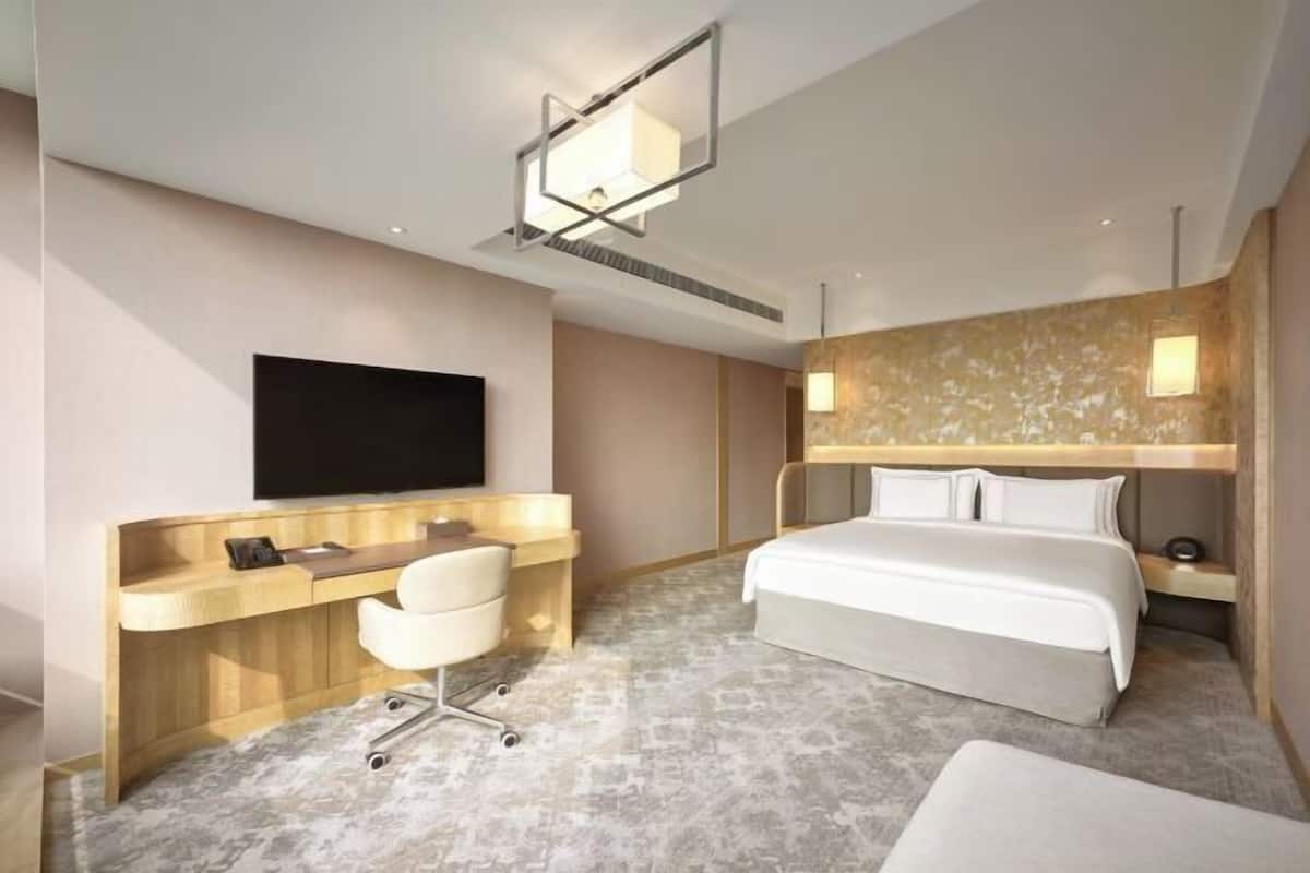 Quarto de hotel moderno com cama, escrivaninha, cadeira, televisão e banheiro.