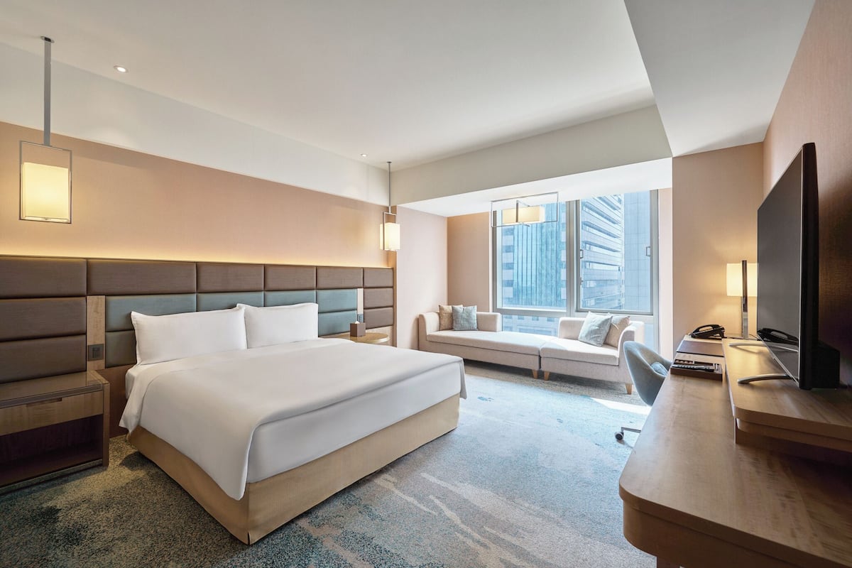 Quarto de hotel moderno com uma cama grande, uma escrivaninha, um sofá e uma televisão.