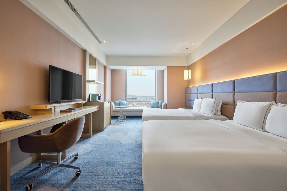 Quarto de hotel com cama, escrivaninha, cadeira, televisão e vista para a cidade.