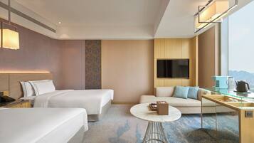 A hotel room with two beds, a sofa, a coffee table, a TV, and a city view.