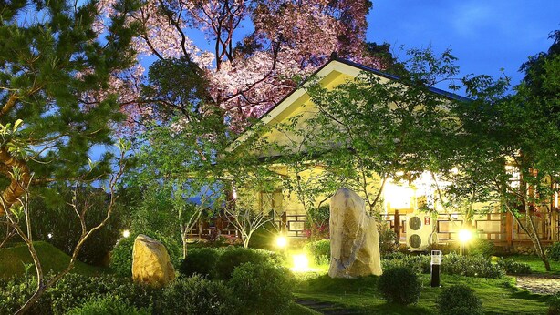 A traditional Japanese-style building with a large cherry blossom tree in the background, surrounded by well-maintained gardens and stone lanterns. - Flying Villa (Puli)
