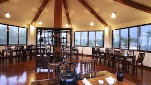 A spacious dining area with wooden tables and chairs, large windows, and a traditional tea set displayed on a table. - Flying Villa (Puli)