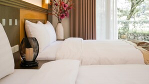 A hotel room with a bed, a bedside table with a lamp, a vase with flowers, and a window with a view of trees. - Flying Villa (Puli)