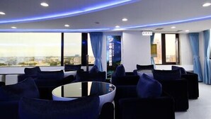 A modern lounge area with a round glass table surrounded by dark blue sofas, large windows with blue curtains, and a city view. - Season Skyline (Luodong)