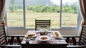 A dining table with plates of food and wine glasses, set against a window with a view of a rural landscape.
