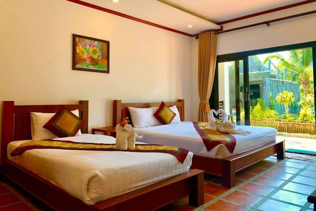 Una camera d'albergo con due letti, un'ampia finestra vista verde e un quadro appeso al muro.