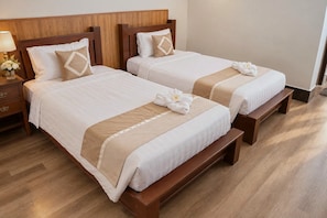 Habitación de hotel con dos camas, cabeceros de madera, una mesita de noche con lámpara y un banco.
