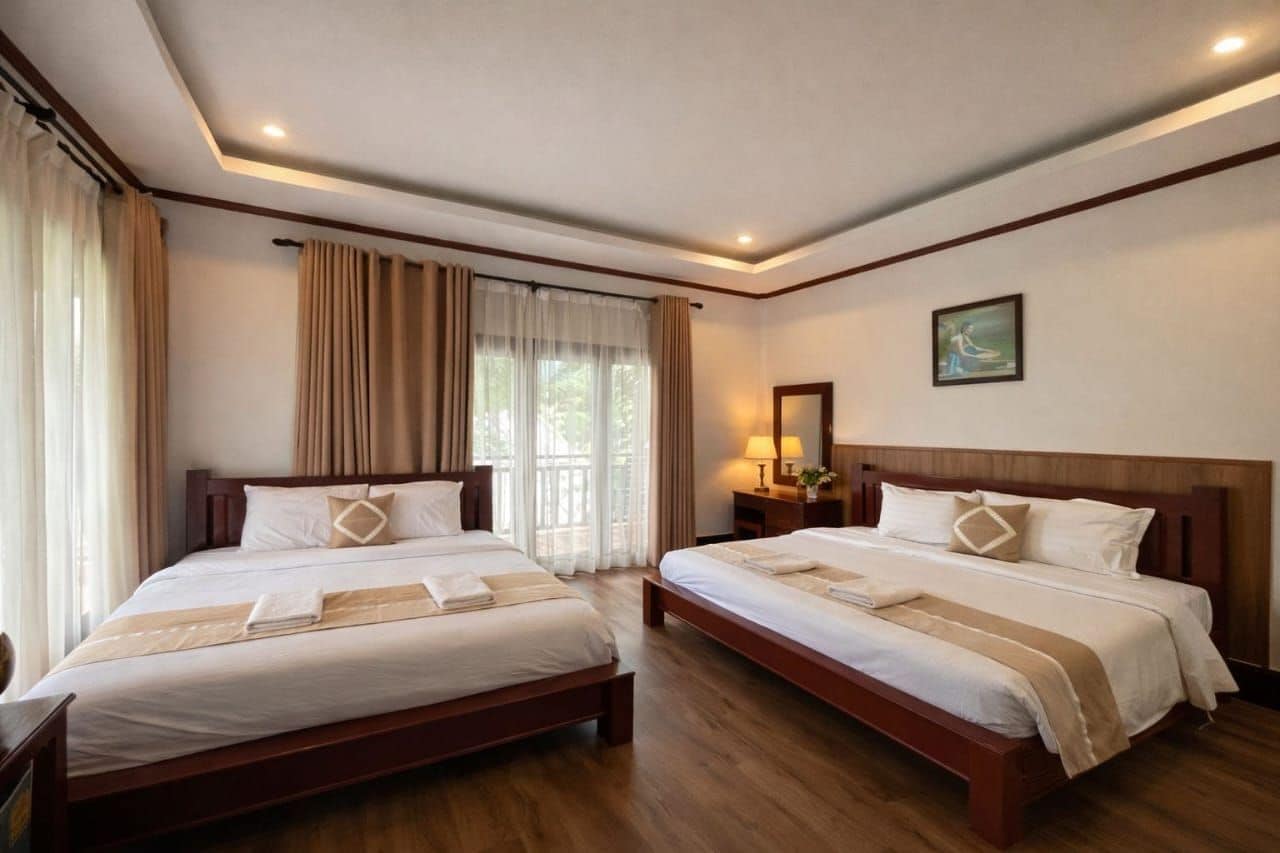 Habitación de hotel con dos camas, un ventanal con cortinas, una mesita de noche con lámpara y un cuadro en la pared.