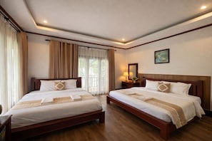 A hotel room with two beds, a large window with curtains, a bedside table with a lamp, and a framed picture on the wall.