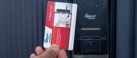 Una mano sostiene una tarjeta cerca de una puerta con lector de tarjetas de acceso y un mecanismo de cierre.