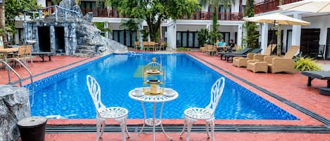 Una piscina con sillas blancas y una mesa, rodeada de sillones de descanso y una palmera.