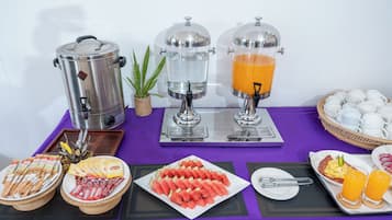 Montaje de un bufé de desayuno con máquinas de café, dispensadores de jugo y una variedad de alimentos.
