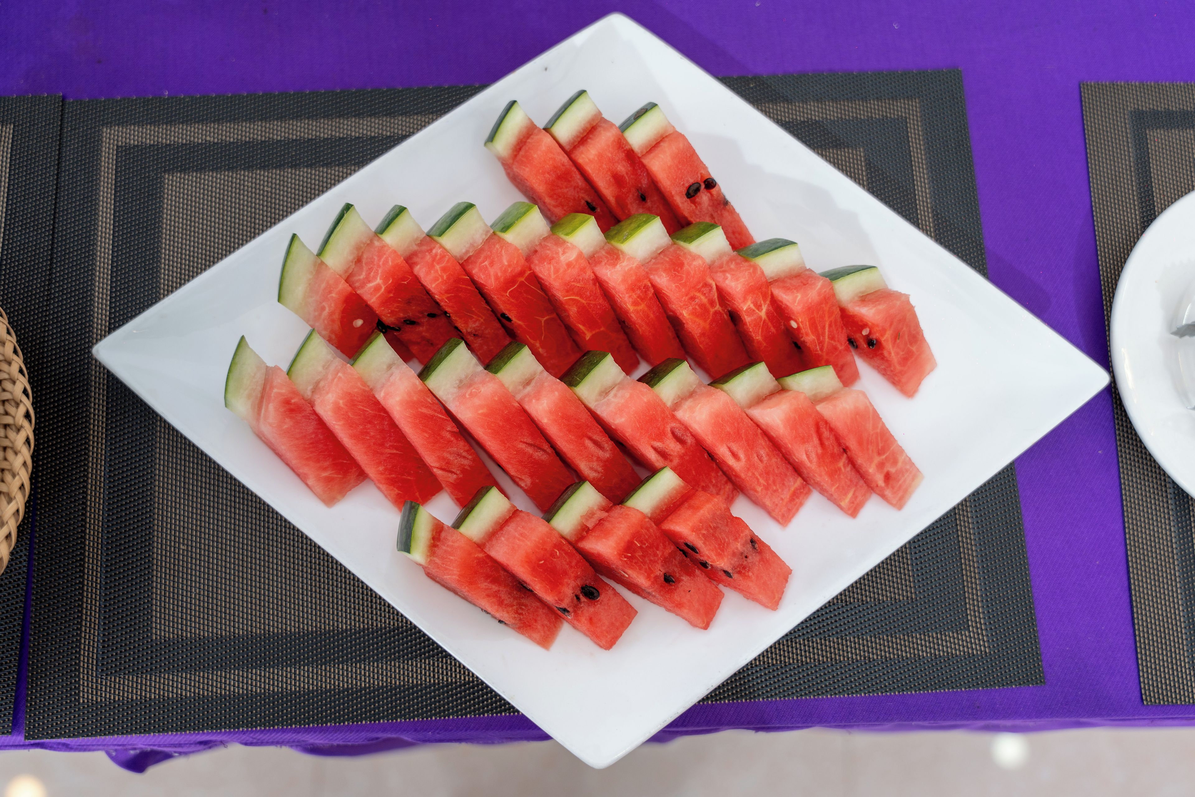 A white plate with neatly arranged watermelon slices and cucumber pieces on a purple placemat.